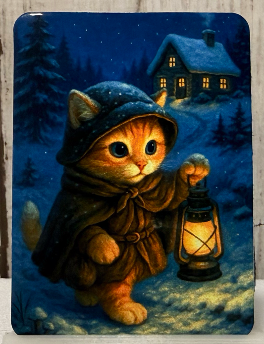 Magnet featuring a cat in a hood and coat holding a lantern in a snowy landscape with a house in the background.