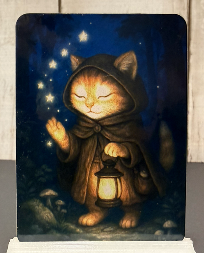 Magnet featuring a cat in a hooded cloak holding a lantern with stars in the background