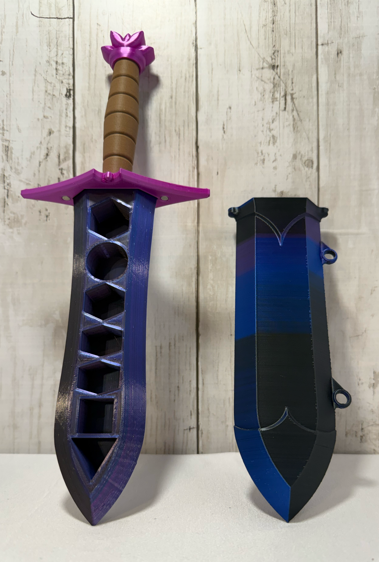 3D-printed dice sword with purple blade, pink pommel, brown handle, and matching sheath.