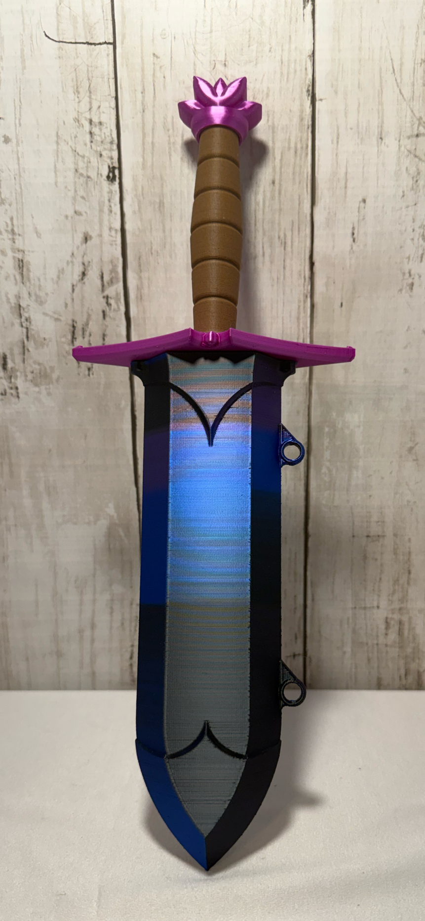 3D-printed dice sword with purple blade, pink pommel, brown handle, and matching sheath.
