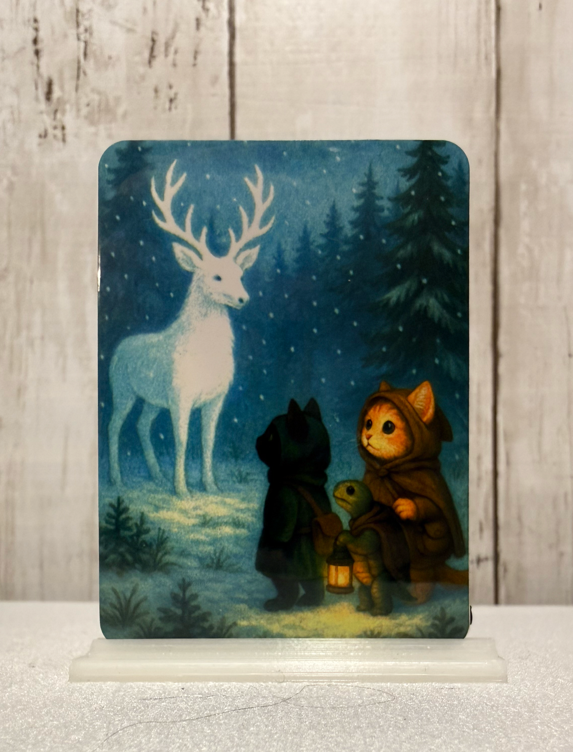 A magnet featuring two cats and a turtle who encounter a winter spirit shaped like a deer.